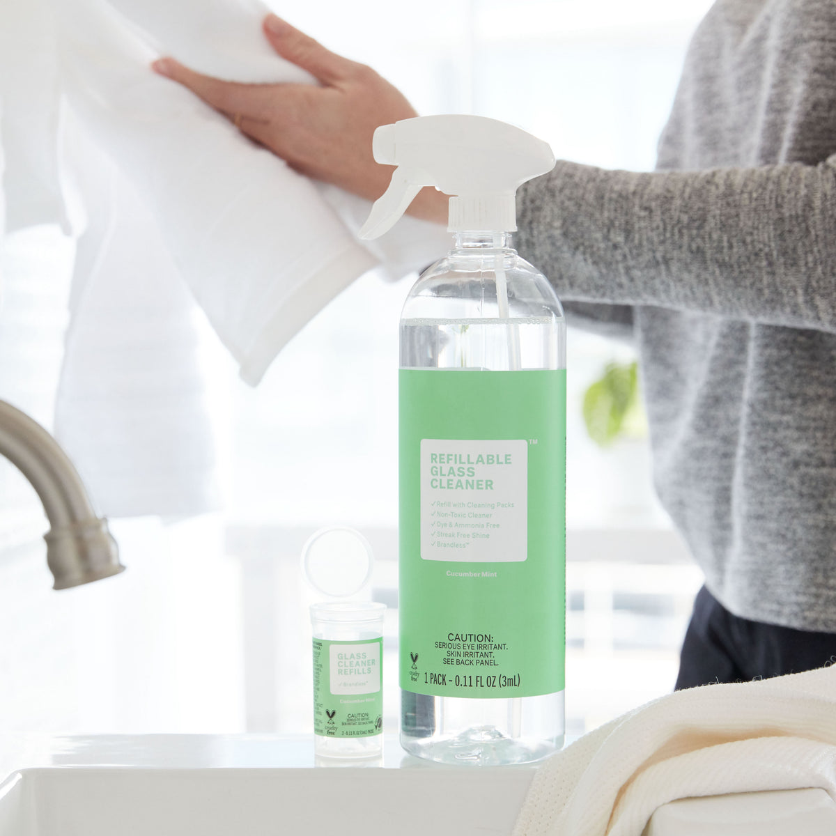 Lifestyle shot of glass cleaner in spray bottle with refills next to it