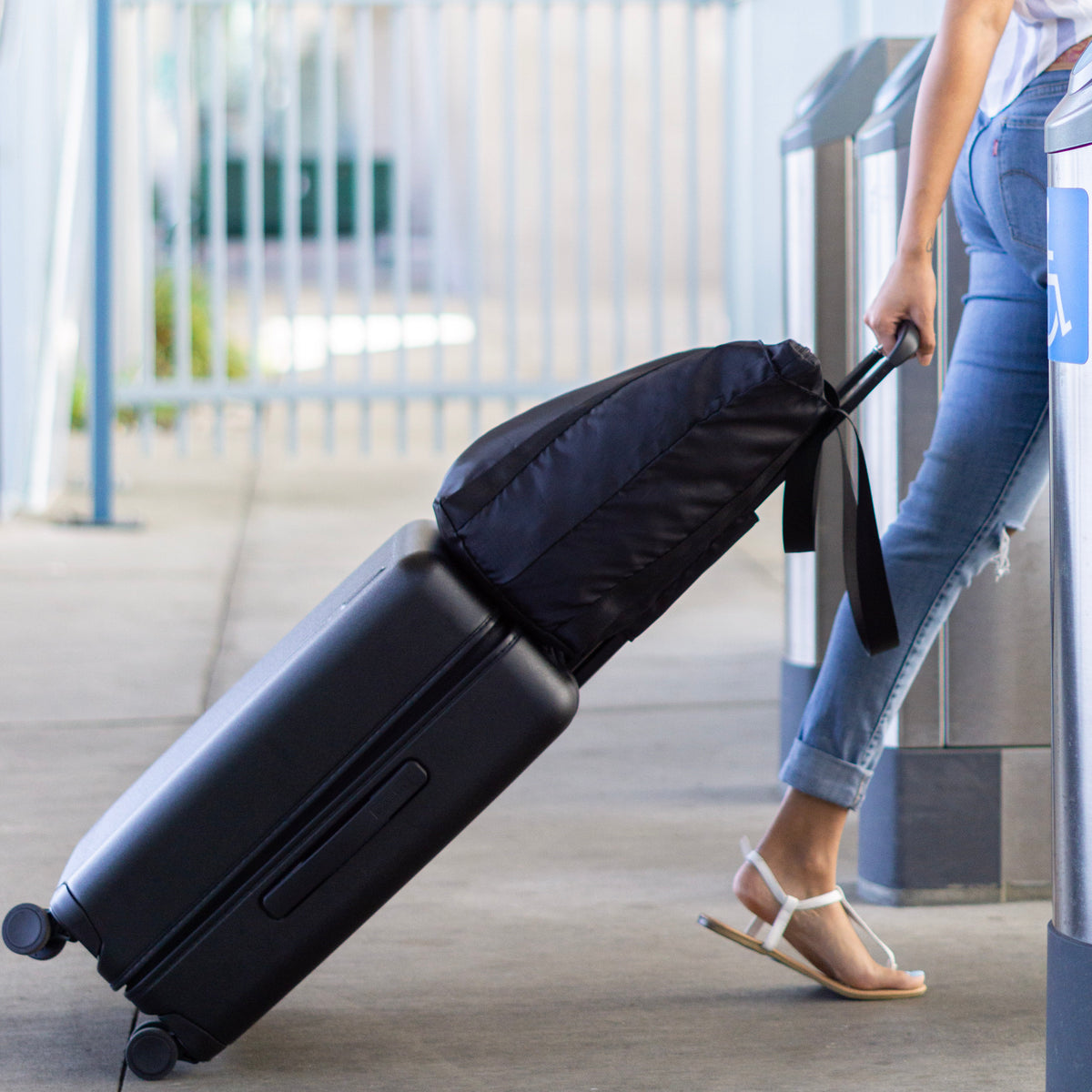 Woman using a single hand to effortlessly carry the Foldable Tote Gag on top of a piece of rolling luggage by using the integrated trolley-handle strap to securely hold the tote bag on top showing how convenient a travel accessory the tote bag can be, taking a load off your shoulder and keeping you hands free for easy travel.